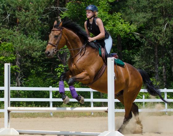 Female student riding a horse over a jump